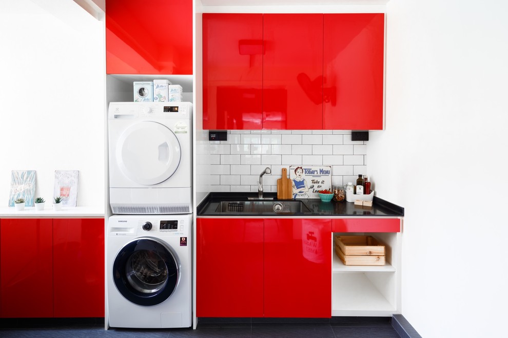 Design ideas for an eclectic utility room in Singapore with an undermount sink, flat-panel cabinets, red cabinets, white walls, a stacked washer and dryer, black floor and black benchtop.