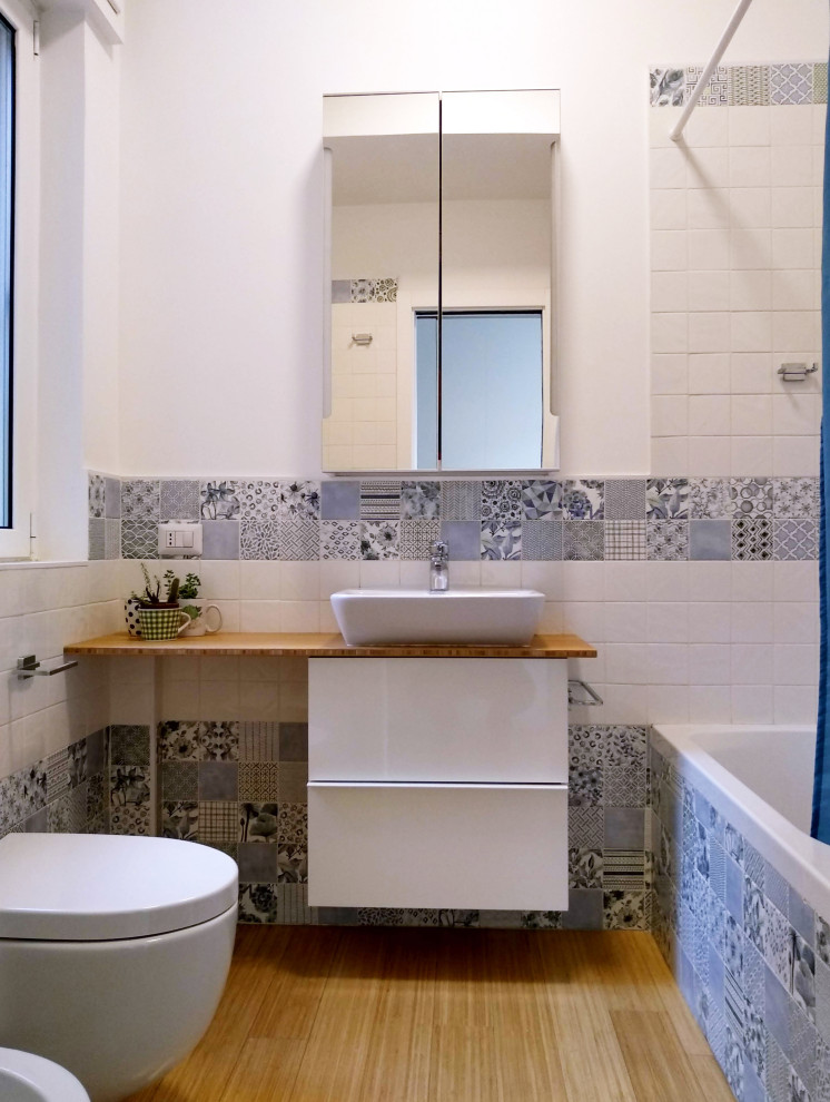 This is an example of a mid-sized traditional 3/4 bathroom in Rome with white cabinets, a corner shower, a two-piece toilet, multi-coloured tile, porcelain tile, multi-coloured walls, light hardwood floors, beige floor, a sliding shower screen, white benchtops, a vessel sink and wood benchtops.