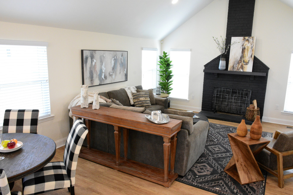 Exemple d'un grand salon nature avec un mur blanc, un sol en vinyl, une cheminée standard, un manteau de cheminée en brique, un téléviseur fixé au mur, un sol marron et un plafond voûté.