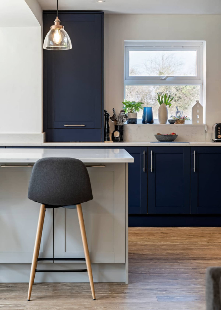 Offene, Große Moderne Küche mit Schrankfronten im Shaker-Stil, blauen Schränken, Quarzit-Arbeitsplatte, Küchenrückwand in Weiß, hellem Holzboden, Kücheninsel, braunem Boden und weißer Arbeitsplatte in Oxfordshire
