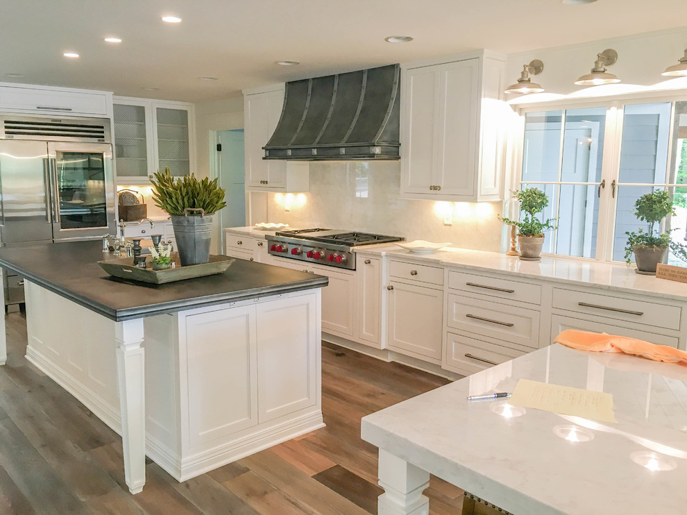Inspiration for an expansive transitional l-shaped kitchen in Other with a farmhouse sink, beaded inset cabinets, white cabinets, zinc benchtops, white splashback, marble splashback, stainless steel appliances, light hardwood floors, multiple islands and brown floor.