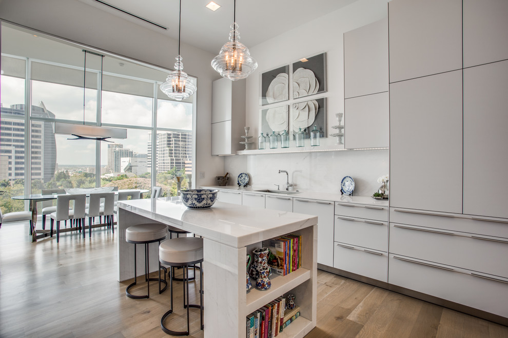 This is an example of a mid-sized contemporary single-wall eat-in kitchen in Dallas with flat-panel cabinets, white cabinets, white splashback, medium hardwood floors, with island, brown floor, white benchtop, an undermount sink and solid surface benchtops.