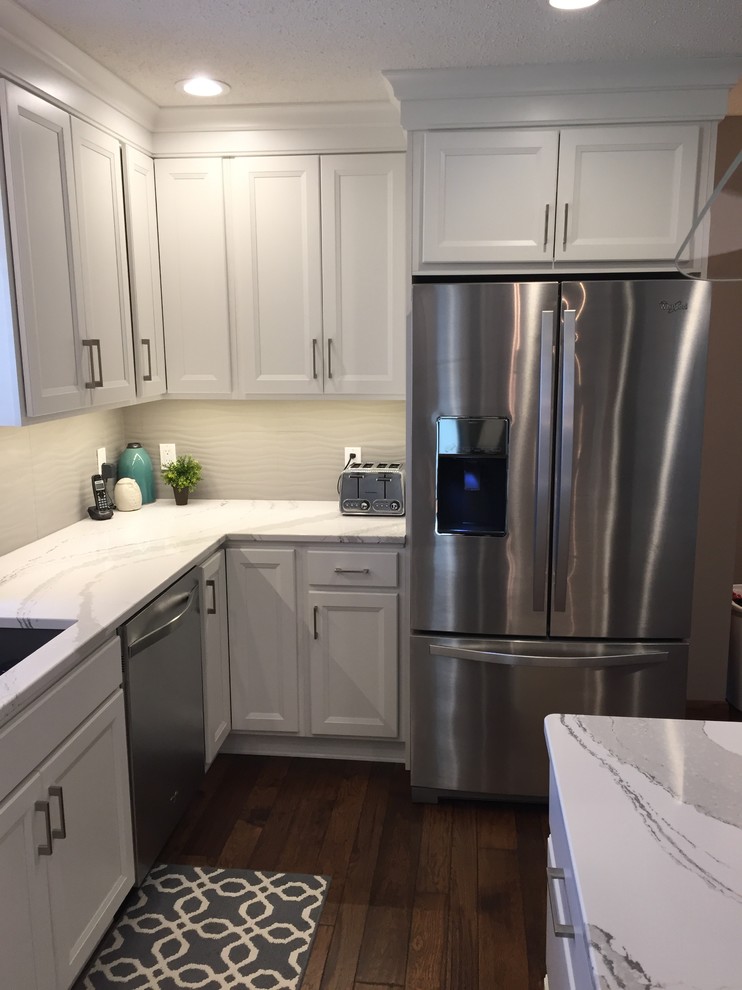 Large transitional l-shaped dark wood floor home design photo with an undermount sink, flat-panel cabinets, white cabinets, quartz countertops, white backsplash, ceramic backsplash, stainless steel appliances and an island
