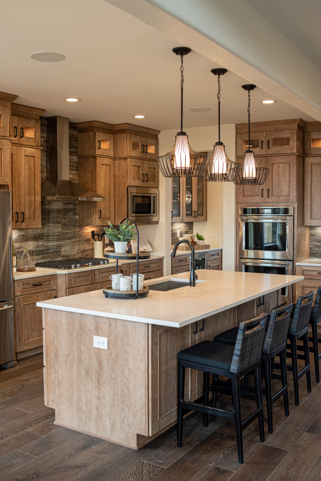 Design ideas for a mid-sized country l-shaped kitchen in Denver with an undermount sink, recessed-panel cabinets, medium wood cabinets, grey splashback, stainless steel appliances, medium hardwood floors, with island, brown floor and beige benchtop.