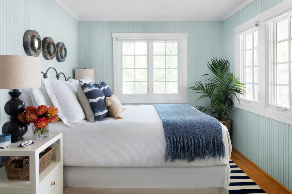 Diseño de dormitorio costero con paredes azules, suelo de madera en tonos medios, suelo marrón y panelado