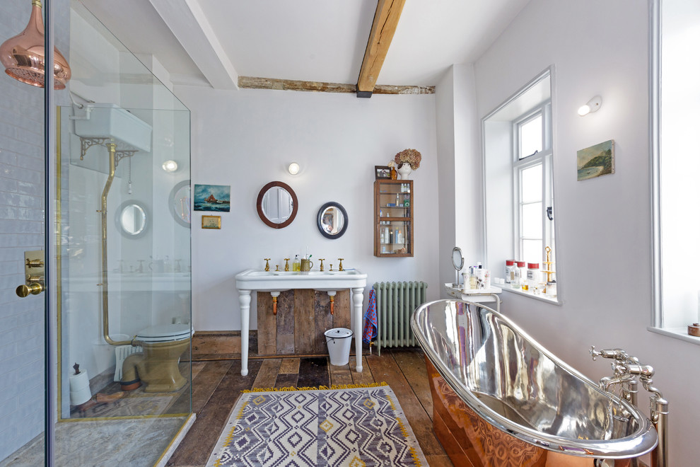 Inspiration for an eclectic bathroom in Oxfordshire with a hinged shower door, a freestanding tub, a two-piece toilet, white tile, white walls, medium hardwood floors, a pedestal sink and brown floor.