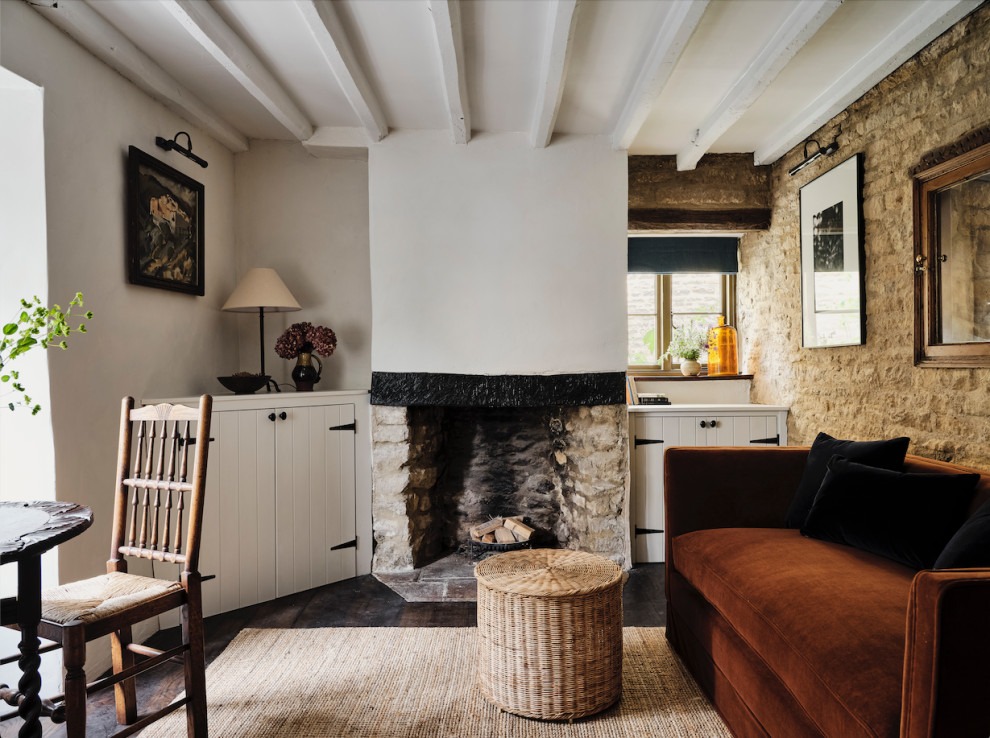 Aménagement d'un petit salon campagne fermé avec un mur blanc, parquet foncé, une cheminée standard, un manteau de cheminée en pierre, un téléviseur dissimulé, un sol marron et poutres apparentes.