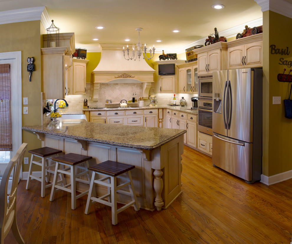 This is an example of a country u-shaped kitchen in New Orleans with a farmhouse sink, raised-panel cabinets, stone tile splashback, stainless steel appliances, light hardwood floors and a peninsula.