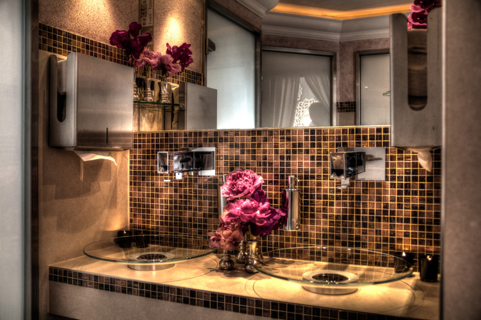 Bild på ett stort vintage beige beige toalett, med en vägghängd toalettstol, brun kakel, glaskakel, beige väggar, linoleumgolv, ett fristående handfat, bänkskiva i glas och orange golv