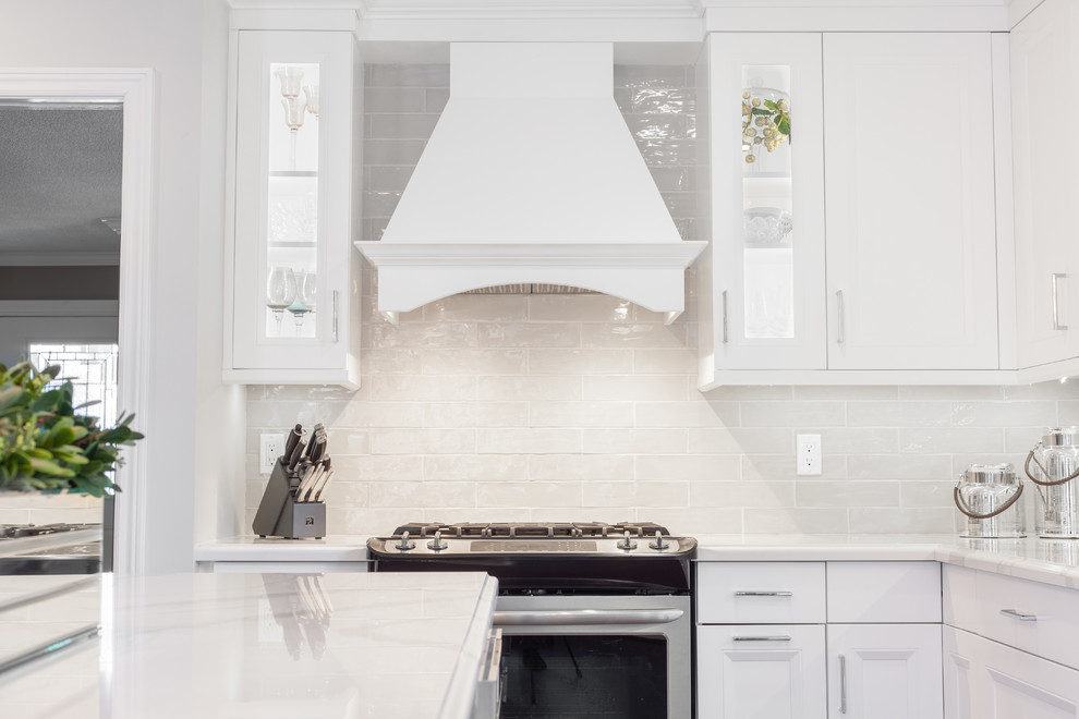 Large transitional l-shaped medium tone wood floor and brown floor enclosed kitchen photo with an undermount sink, recessed-panel cabinets, white cabinets, quartz countertops, gray backsplash, ceramic backsplash, stainless steel appliances, an island and white countertops
