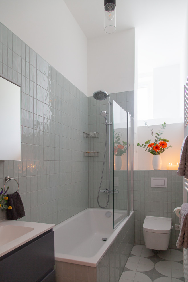 Идея дизайна: узкая и длинная серо-белая ванная комната среднего размера в современном стиле с фасадами с выступающей филенкой, серыми фасадами, накладной ванной, душем над ванной, раздельным унитазом, зеленой плиткой, керамической плиткой, белыми стенами, полом из керамической плитки, душевой кабиной, монолитной раковиной, столешницей из ламината, серым полом, открытым душем, белой столешницей, тумбой под одну раковину, подвесной тумбой и многоуровневым потолком