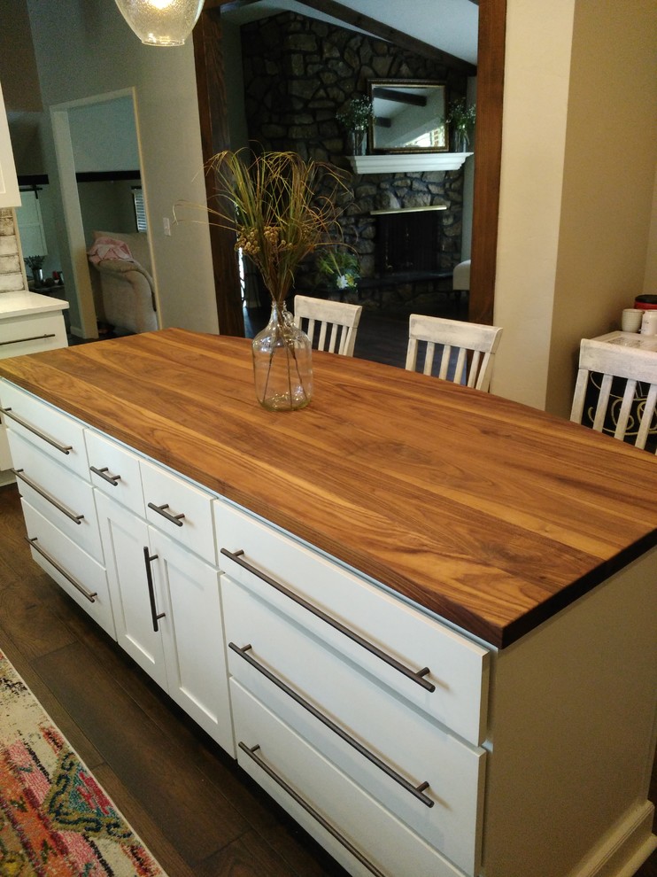Mid-sized transitional l-shaped dark wood floor and brown floor eat-in kitchen photo with shaker cabinets, white cabinets, wood countertops, an island, a farmhouse sink, gray backsplash, marble backsplash and stainless steel appliances