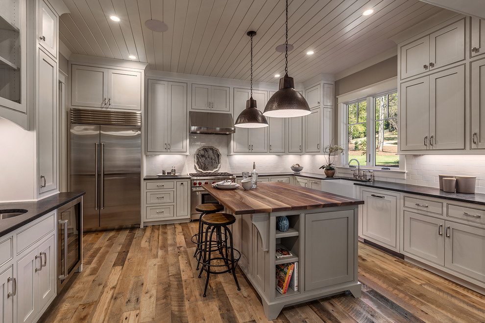 Inspiration for a mid-sized rustic l-shaped light wood floor open concept kitchen remodel with a farmhouse sink, recessed-panel cabinets, white cabinets, granite countertops, white backsplash, subway tile backsplash, stainless steel appliances and an island