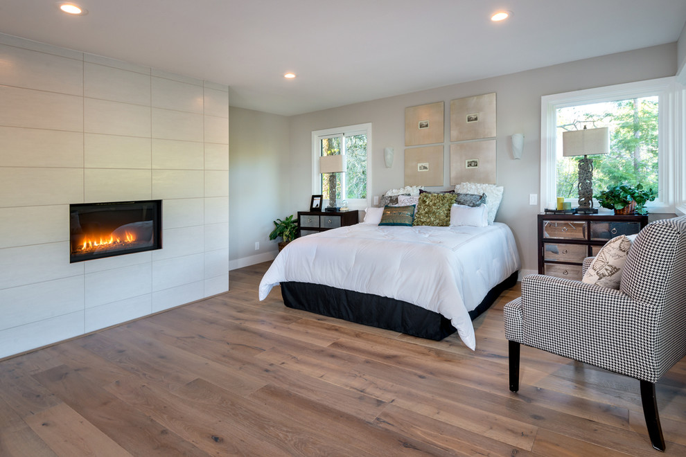 Large modern master bedroom in San Francisco with grey walls, light hardwood floors, a standard fireplace, a tile fireplace surround and grey floor.
