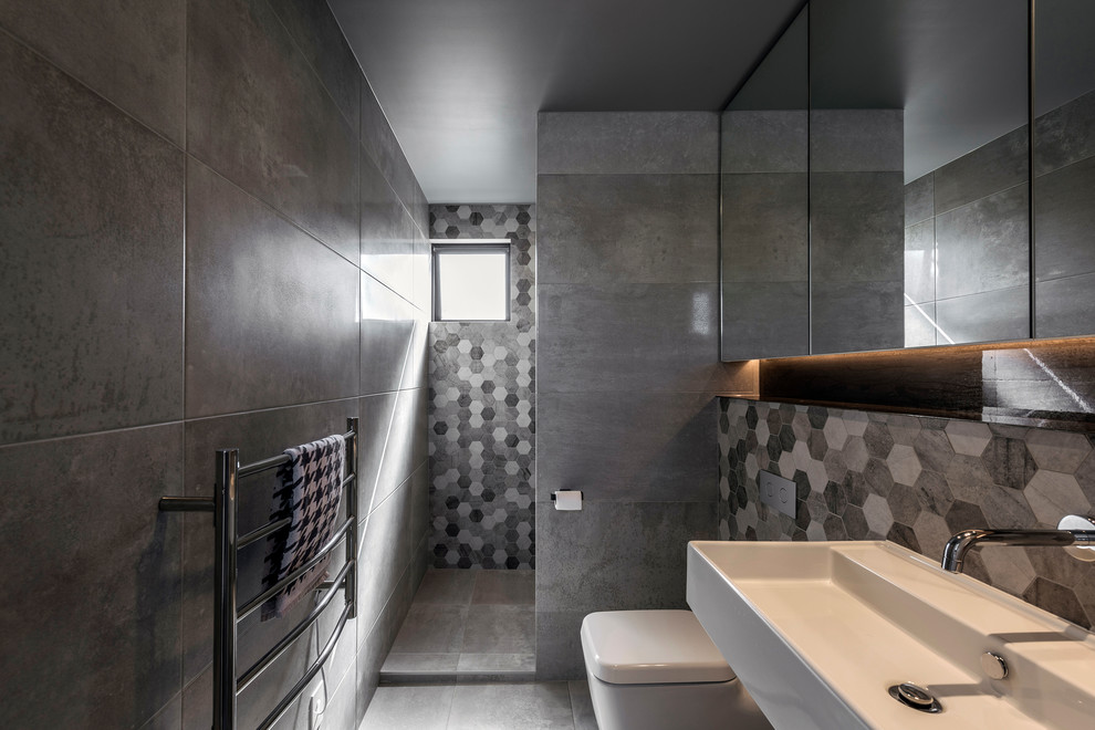 Small modern wet room bathroom in Christchurch with a wall-mount toilet, gray tile, porcelain tile, grey walls, porcelain floors, a wall-mount sink, grey floor and an open shower.
