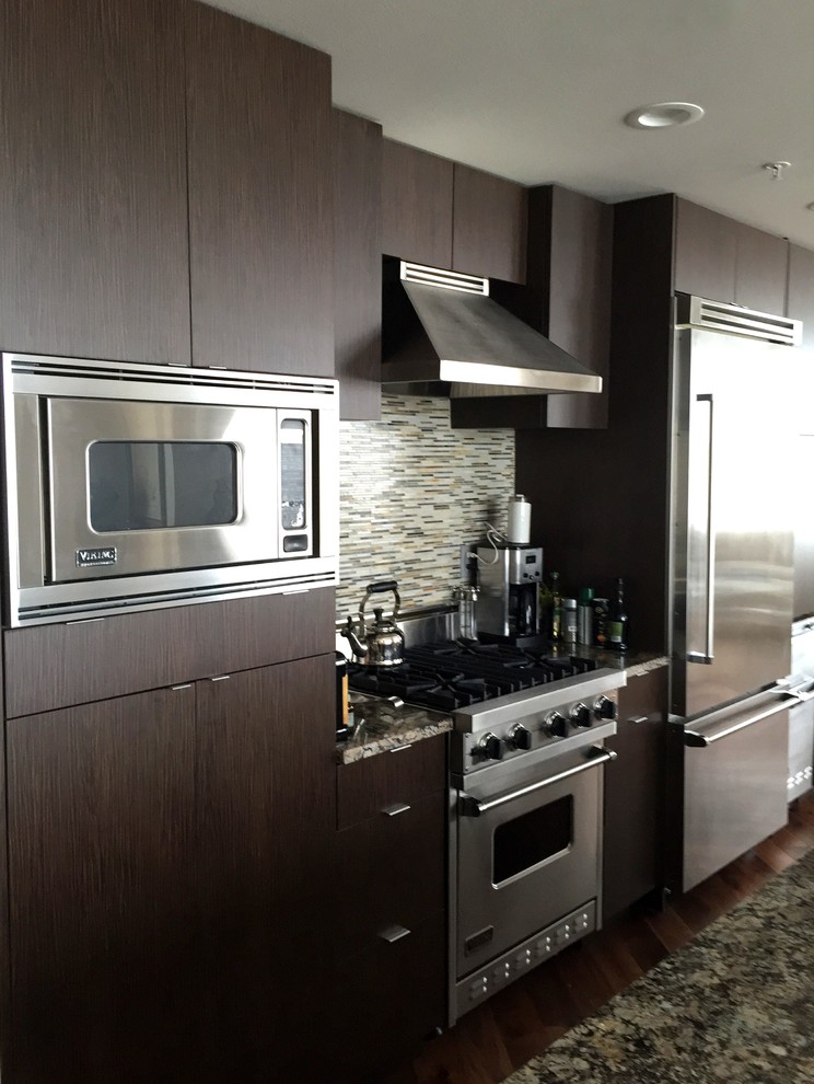 This is an example of a mid-sized modern single-wall open plan kitchen in Tampa with a drop-in sink, flat-panel cabinets, dark wood cabinets, granite benchtops, multi-coloured splashback, ceramic splashback, stainless steel appliances, medium hardwood floors, with island and multi-coloured benchtop.