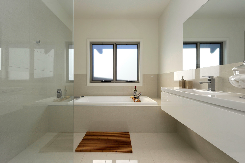 Inspiration for a mid-sized contemporary kids bathroom in Newcastle - Maitland with white cabinets, a drop-in tub, an open shower, beige tile, porcelain tile, beige walls, porcelain floors, an integrated sink and engineered quartz benchtops.