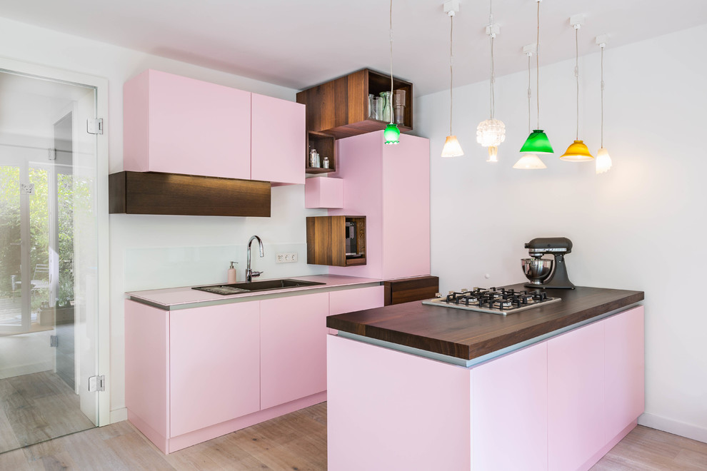 This is an example of an eclectic kitchen in Cologne with a drop-in sink, flat-panel cabinets, white splashback, light hardwood floors, glass sheet splashback, a peninsula, beige floor and pink benchtop.