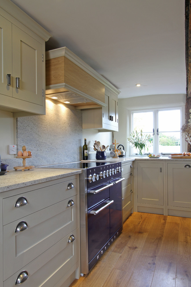 Design ideas for a large country l-shaped eat-in kitchen in Hampshire with shaker cabinets, beige cabinets, coloured appliances, granite benchtops, white splashback, stone slab splashback, a farmhouse sink, dark hardwood floors and with island.