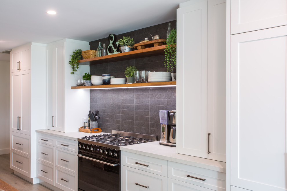 Photo of an expansive country galley eat-in kitchen in Brisbane with a double-bowl sink, recessed-panel cabinets, black cabinets, wood benchtops, black splashback, subway tile splashback, black appliances, with island, grey floor and white benchtop.