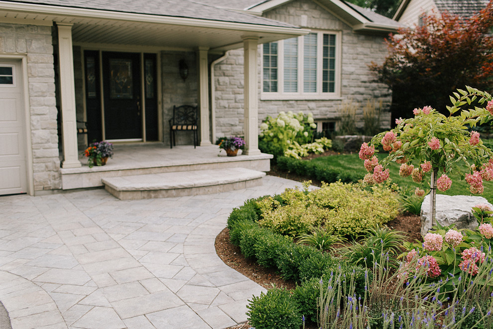 This is an example of a mid-sized traditional front yard full sun driveway for summer in Toronto with concrete pavers.