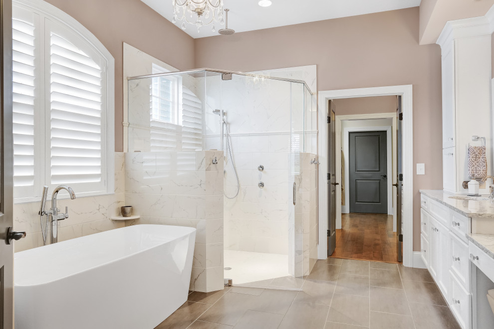 This is an example of a beach style master bathroom in Wilmington with white cabinets, a freestanding tub, a curbless shower, white tile, ceramic tile, beige walls, ceramic floors, granite benchtops, beige floor, a hinged shower door and multi-coloured benchtops.