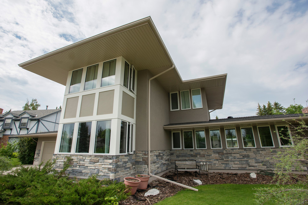 Photo of a large modern two-storey stucco beige house exterior in Calgary with a flat roof and a shingle roof.