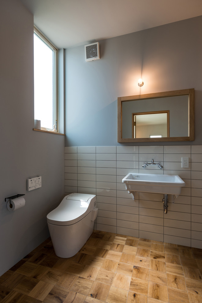 Inspiration for an industrial powder room in Other with white tile, multi-coloured walls, medium hardwood floors, a wall-mount sink and brown floor.