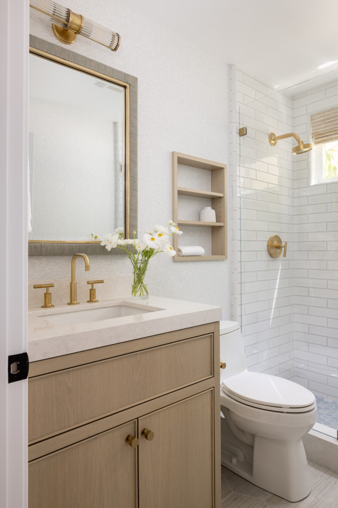 This is an example of a small beach style 3/4 bathroom in Orange County with beaded inset cabinets, beige cabinets, an alcove shower, a one-piece toilet, white tile, porcelain tile, grey walls, porcelain floors, an undermount sink, engineered quartz benchtops, green floor, a hinged shower door, white benchtops, a niche, a single vanity, a built-in vanity and wallpaper.