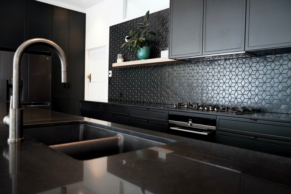 This is an example of a large modern l-shaped open plan kitchen in Sydney with an undermount sink, shaker cabinets, black cabinets, quartz benchtops, black splashback, mosaic tile splashback, black appliances, ceramic floors, with island, green floor and black benchtop.