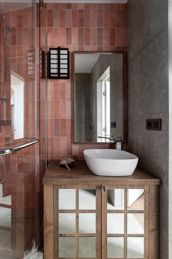На фото: главная ванная комната среднего размера в восточном стиле с стеклянными фасадами, темными деревянными фасадами, угловым душем, инсталляцией, розовой плиткой, керамической плиткой, розовыми стенами, полом из керамогранита, накладной раковиной, столешницей из ламината, серым полом, душем с распашными дверями, коричневой столешницей, зеркалом с подсветкой, тумбой под одну раковину, напольной тумбой, балками на потолке и панелями на части стены