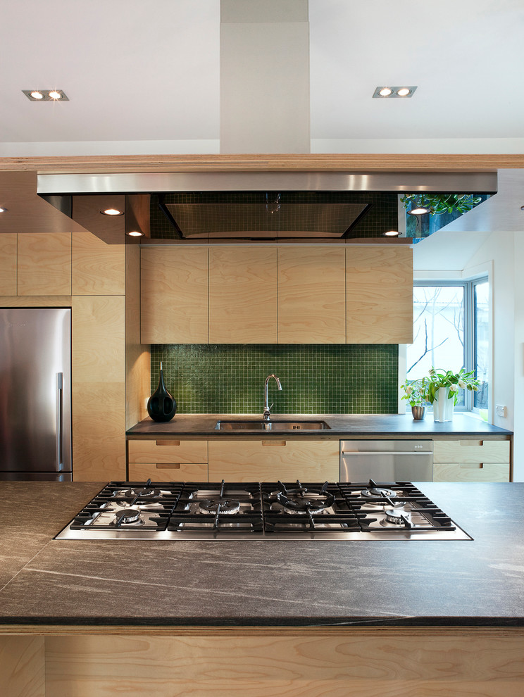 Photo of a mid-sized contemporary galley eat-in kitchen in Auckland with a drop-in sink, flat-panel cabinets, light wood cabinets, quartzite benchtops, green splashback, glass tile splashback, stainless steel appliances, medium hardwood floors and with island.