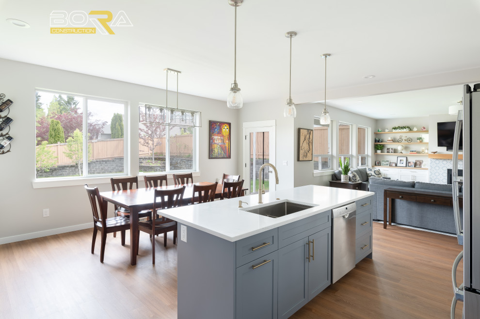 Large transitional l-shaped medium tone wood floor and brown floor eat-in kitchen photo in Seattle with an undermount sink, shaker cabinets, blue cabinets, quartz countertops, white backsplash, ceramic backsplash, stainless steel appliances, an island and white countertops