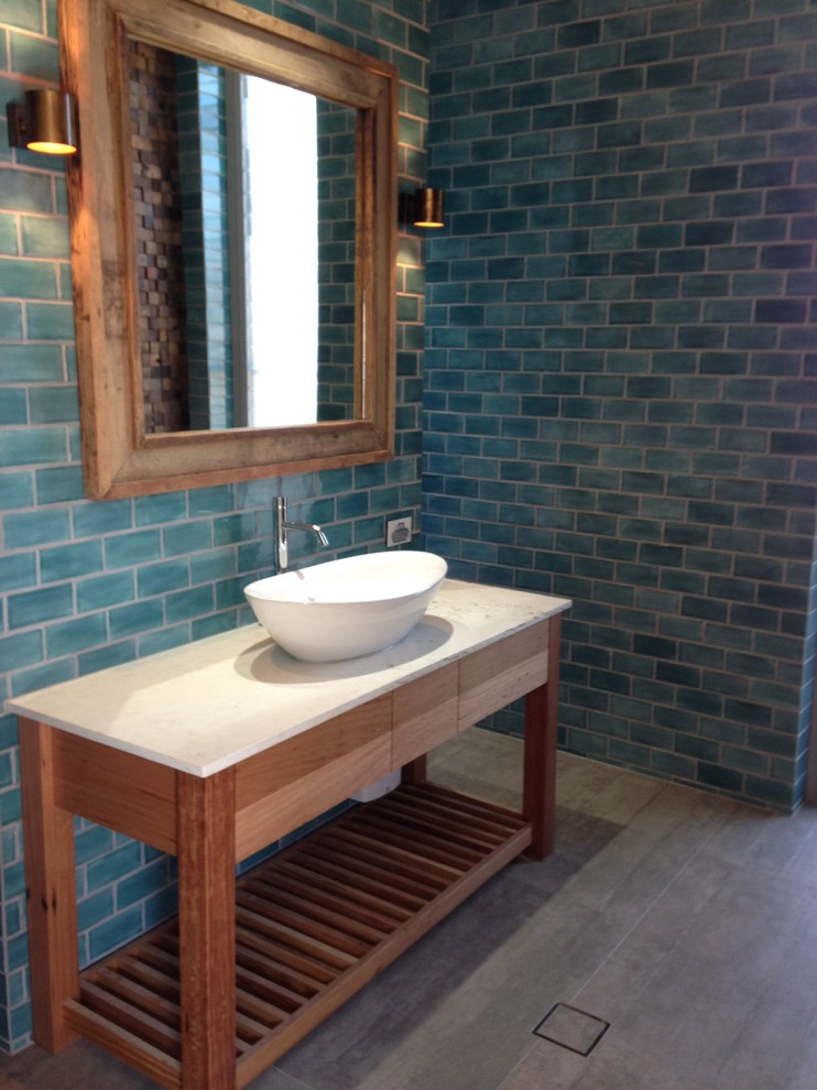 Inspiration for a beach style bathroom in Sunshine Coast with a vessel sink, furniture-like cabinets, medium wood cabinets, limestone benchtops, blue tile, porcelain tile, blue walls and porcelain floors.
