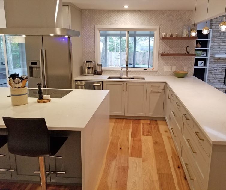 Design ideas for a mid-sized contemporary l-shaped eat-in kitchen in Austin with a triple-bowl sink, recessed-panel cabinets, grey cabinets, quartz benchtops, grey splashback, marble splashback, stainless steel appliances, light hardwood floors, with island and white benchtop.