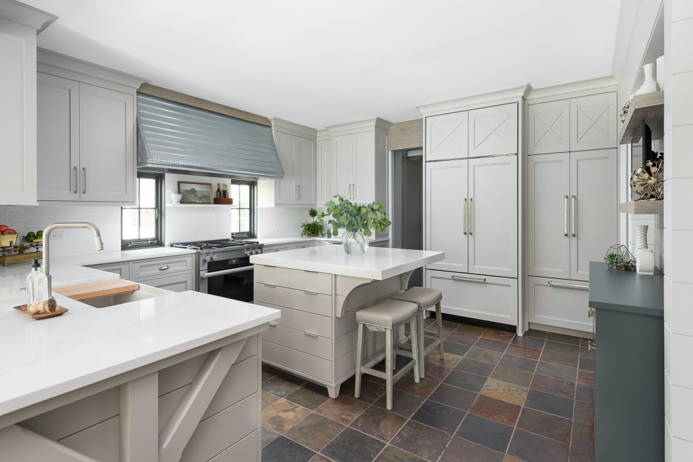 Inspiration for a mid-sized transitional u-shaped eat-in kitchen in Chicago with a farmhouse sink, flat-panel cabinets, grey cabinets, quartz benchtops, white splashback, subway tile splashback, panelled appliances, slate floors, with island, white benchtop and multi-coloured floor.