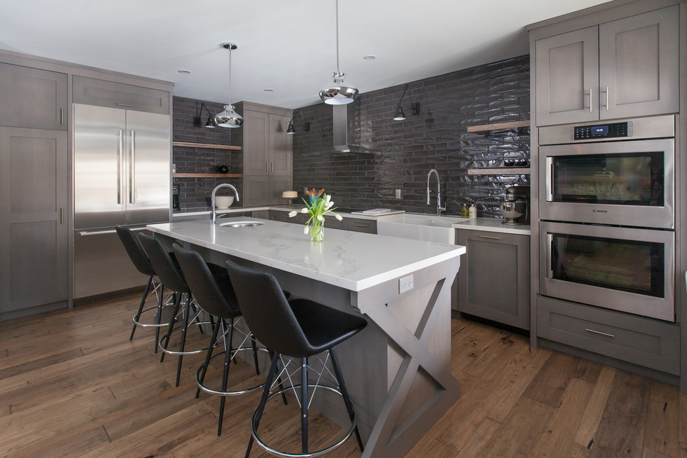 Mid-sized contemporary kitchen in Toronto with a farmhouse sink, shaker cabinets, grey cabinets, marble benchtops, grey splashback, subway tile splashback, stainless steel appliances, medium hardwood floors and with island.