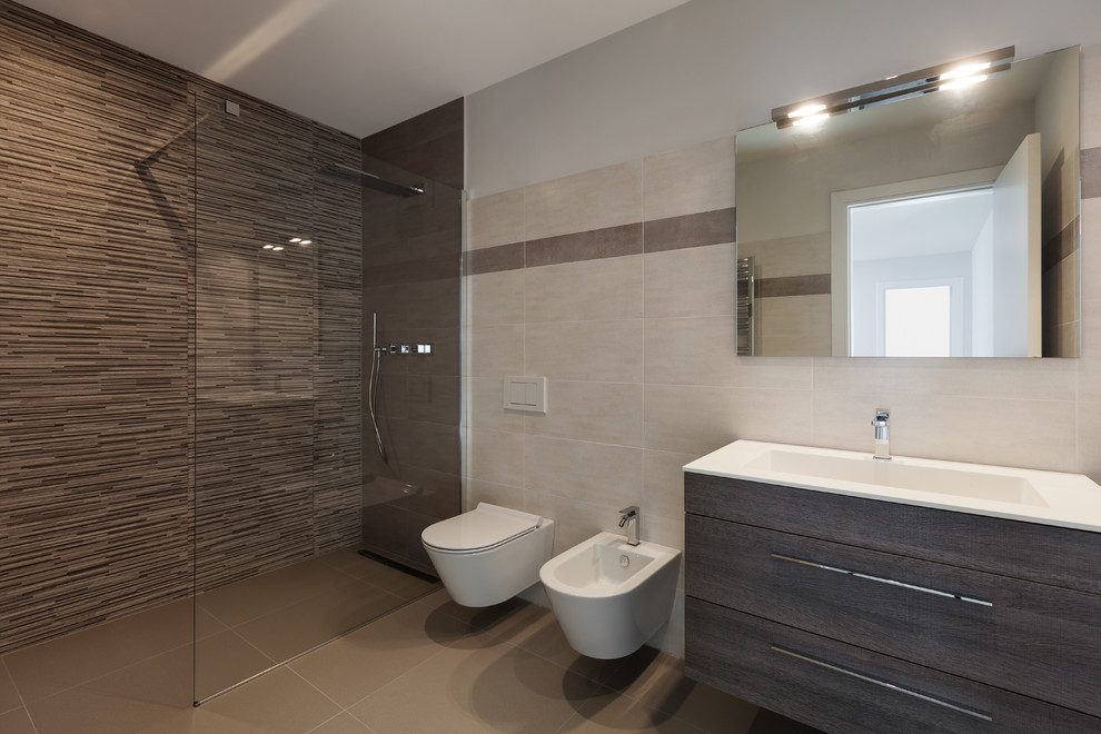 This is an example of a large contemporary master bathroom in Melbourne with dark wood cabinets, an open shower, porcelain tile, porcelain floors, a vessel sink, solid surface benchtops, an open shower, a bidet, beige tile, beige walls and brown floor.