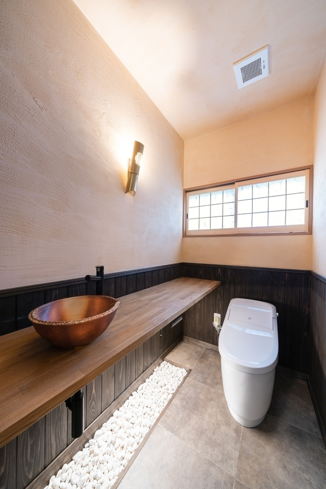 Photo of an asian powder room in Tokyo with white walls, a vessel sink, wood benchtops, grey floor and brown benchtops.