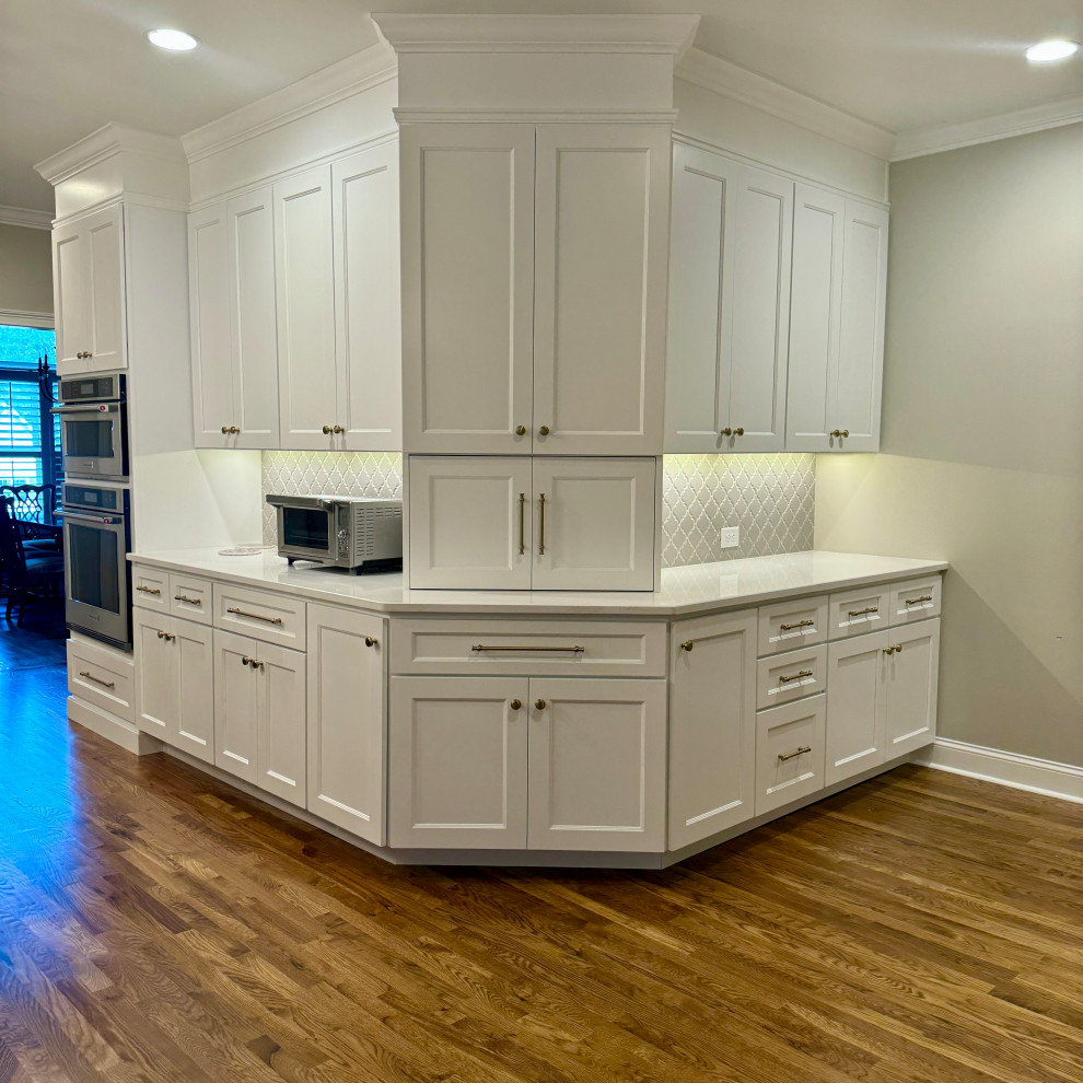 Example of a mid-sized transitional l-shaped medium tone wood floor, brown floor and wallpaper ceiling eat-in kitchen design in Atlanta with a double-bowl sink, shaker cabinets, white cabinets, granite countertops, gray backsplash, mosaic tile backsplash, stainless steel appliances, an island and white countertops
