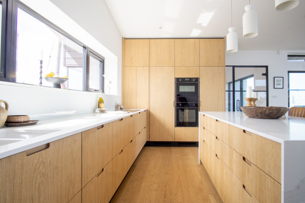 Design ideas for a large scandinavian l-shaped open plan kitchen with a double-bowl sink, flat-panel cabinets, light wood cabinets, marble worktops, black appliances, an island and beige worktops.
