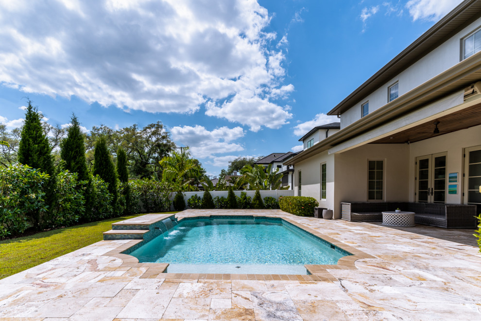 This is an example of a medium sized eclectic back custom shaped swimming pool in Tampa with with pool landscaping and natural stone paving.