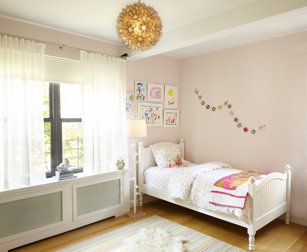 Photo of a mid-sized transitional kids' bedroom for girls and kids 4-10 years old in New York with pink walls and light hardwood floors.