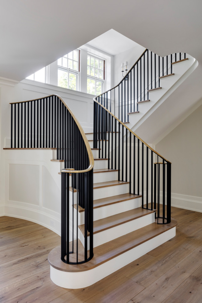 На фото: большая винтовая деревянная лестница в классическом стиле с деревянными ступенями, металлическими перилами и панелями на стенах с