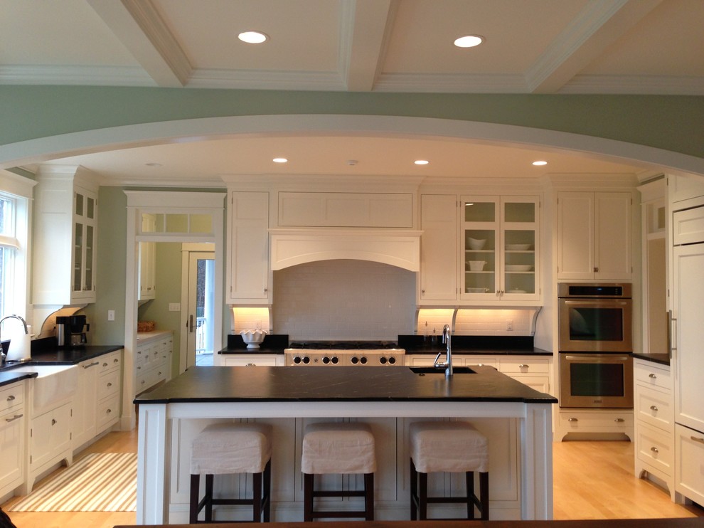 Design ideas for a large traditional u-shaped eat-in kitchen in Portland Maine with a farmhouse sink, beaded inset cabinets, white cabinets, soapstone benchtops, white splashback, subway tile splashback, stainless steel appliances, light hardwood floors and with island.