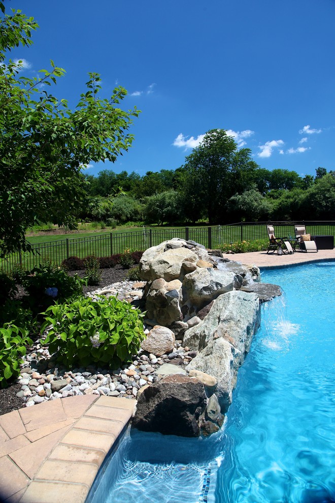 Photo of a mid-sized country backyard custom-shaped pool in New York with a water feature and brick pavers.