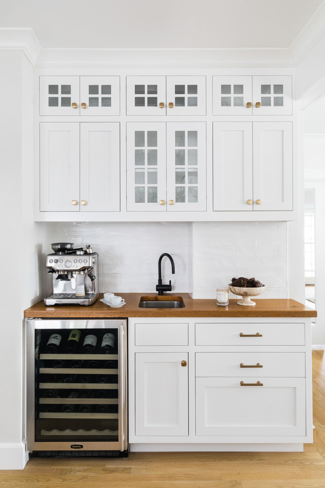 This is an example of a small traditional single-wall wet bar in Boston with an undermount sink, white cabinets, wood benchtops, white splashback, light hardwood floors, subway tile splashback, brown benchtop and shaker cabinets.