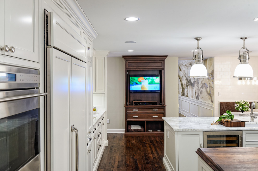 This is an example of a large transitional u-shaped eat-in kitchen in Cleveland with an undermount sink, beaded inset cabinets, white cabinets, marble benchtops, white splashback, ceramic splashback, panelled appliances, dark hardwood floors and multiple islands.