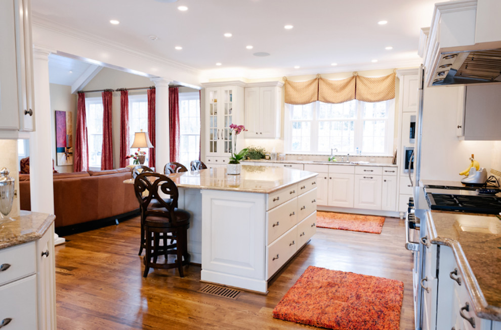 This is an example of a large traditional u-shaped open plan kitchen in Raleigh with a double-bowl sink, flat-panel cabinets, white cabinets, granite benchtops, white splashback, stainless steel appliances, medium hardwood floors and with island.