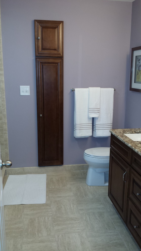 Photo of a mid-sized traditional master bathroom in Philadelphia with raised-panel cabinets, dark wood cabinets, a drop-in tub, a corner shower, a one-piece toilet, beige tile, porcelain tile, purple walls, laminate floors, an undermount sink, granite benchtops, beige floor, a hinged shower door and beige benchtops.